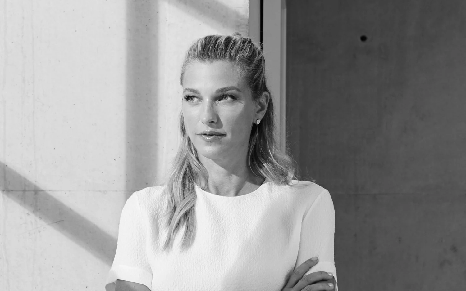 Nicole Junkermann in a white top beside a sunlit concrete wall, a black and white portrait Nicole Junkermann in a white top beside a sunlit concrete wall, a black and white portrait