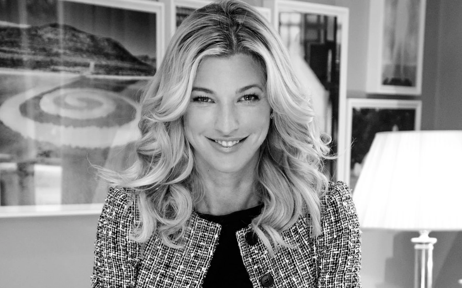 Nicole Junkermann in a tweed jacket, smiling in a room hung with framed pictures, a black and white portrait Nicole Junkermann in a tweed jacket, smiling in a room hung with framed pictures, a black and white portrait